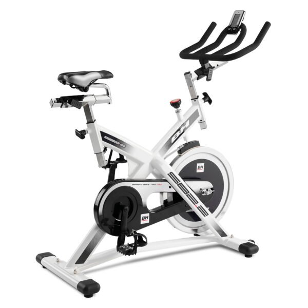 Imagen de una bicicleta tipo indoor bike de color blanco con detalles en negro. Se pueden apreciar las perillas que permiten regular el manubrio y el asiento, tanto en altura como en distancia. El asiento se asemeja al de las bicicletas de carrera. Se observa un monitor que permite hacer un seguimiento del entrenamiento. También se divisa el nombre de la marca 'BH' en varias posiciones.