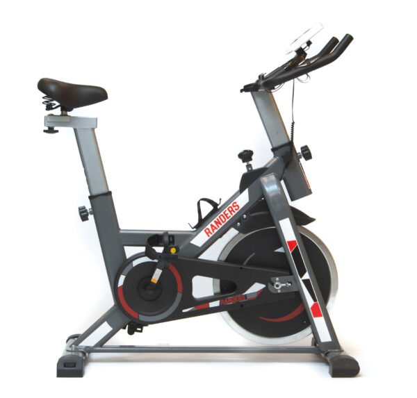 Imagen de una bicicleta fija tipo indoor bike en color gris con detalles en rojo y negro de la marca Randers. El asiento es más amplio de lo habitual y cuenta con resortes para mayor comodidad. Se pueden observar las perillas para ajustar la altura y distancia del asiento, así como el manubrio en altura. Tiene un tablero que permite observar información del entrenamiento. La bicicleta incluye un portacaramañola y en la pata trasera se encuentran perillas para adaptarse a desniveles del suelo.